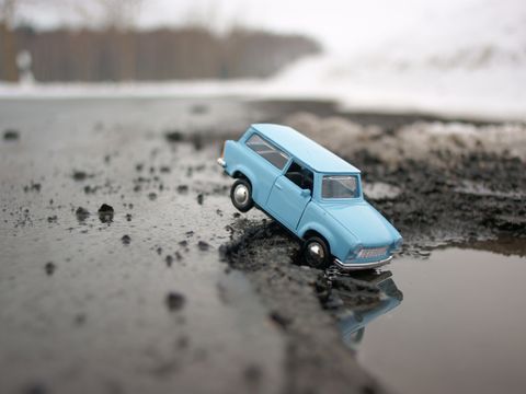 Ein Spielzeugtrabbi der in ein Schlagloch einer asphaltierten Straße hineinfällt