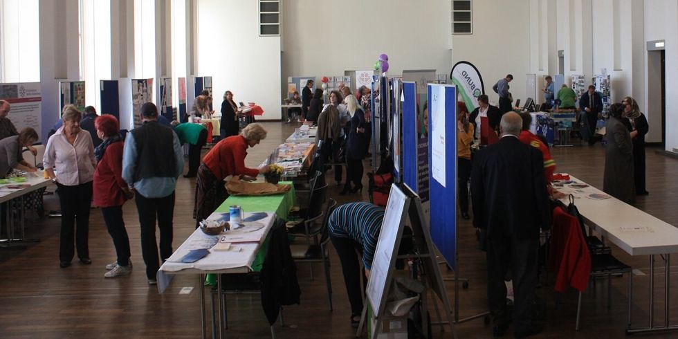 Großer Saal gefüllt mit Menschen und Ständen.