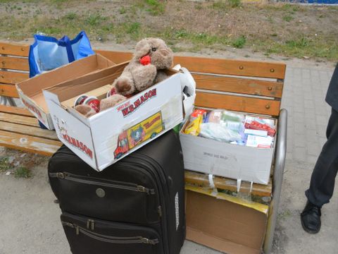 Ein Koffer mit Kleidungsstücken steht an einer Bank. Auf dem Koffer sitzt ein Kuscheltier