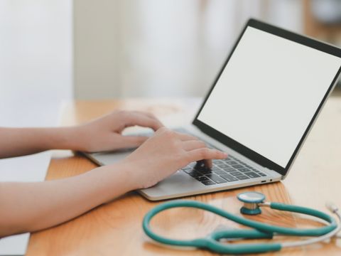 Person tippt auf Laptop, daneben liegt ein Stethoskop