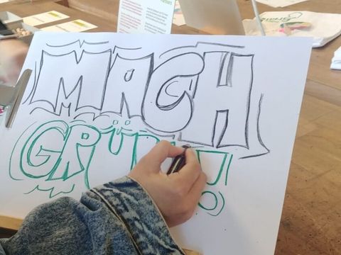 Ein Kind schreibt auf ein Papier "Mach Grün!"