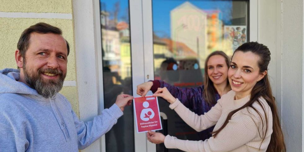 Bezirksstadträtin Weingart und Beschäftigte der Stephanus Stiftung bringen das Plakat "Stillfreundlicher Ort" vor dem Nachbarschaftszentrum an