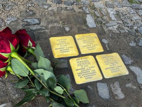 Rote Rosen auf Pflastersteinen neben Stolpersteinen