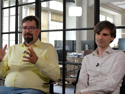 Profilbild von Dominik Bösl und Ronnie Vuine vor Bürohintergrund