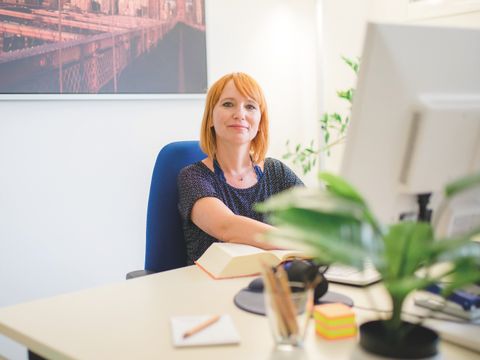 Mitarbeiterin sitzt vor dem PC und schaut in die Kamera