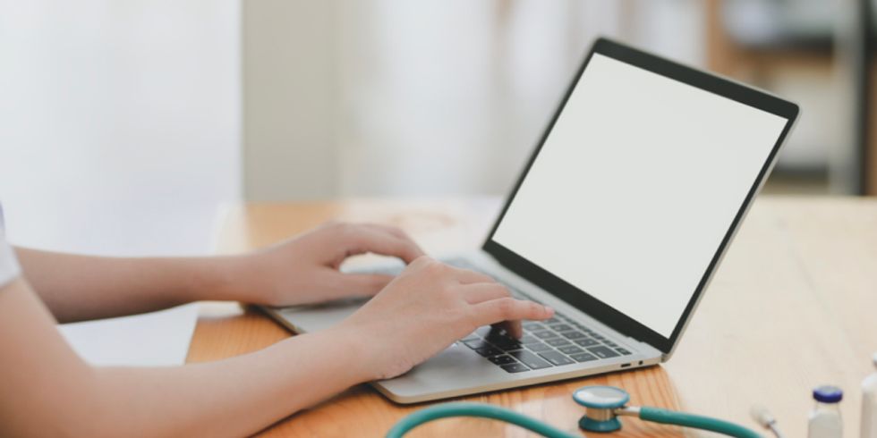 Person tippt auf Laptop, daneben liegt ein Stethoskop