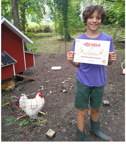 Kind mit einer Urkunde in der Hand daneben ein Huhn