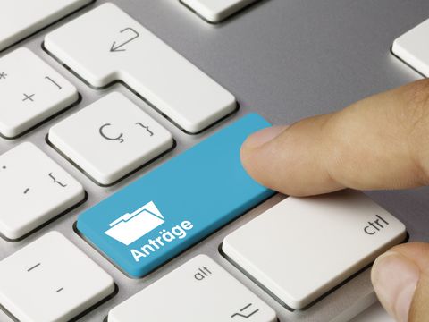 Ausschnitt einer Tastatur mit einer blau hervorgehobeben Taste auf der Anträge steht und von einem Finger berührt wird