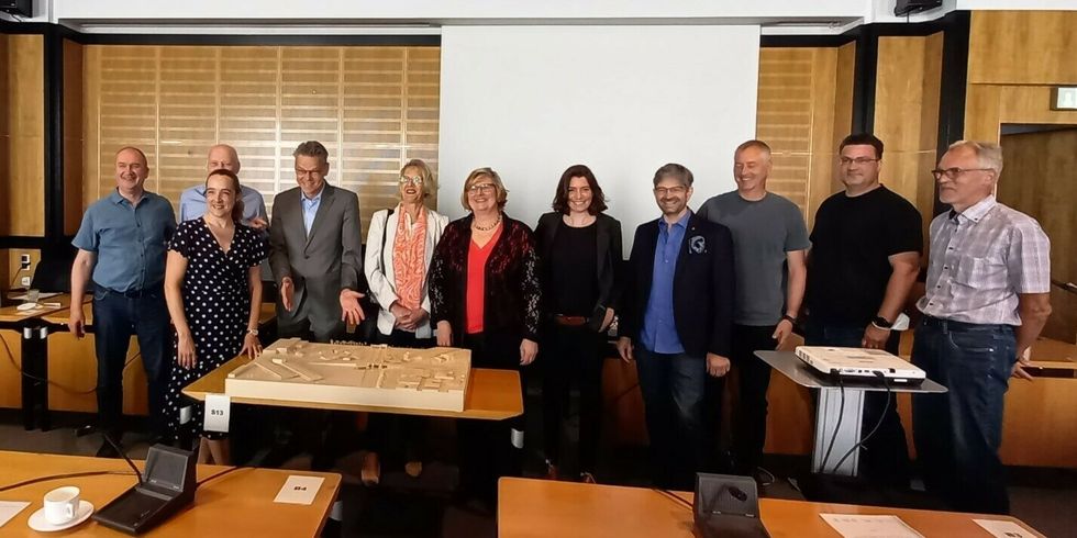 11 Personen stehen in einem Schulungsraum nebeneinander und schauen in die Kamera.