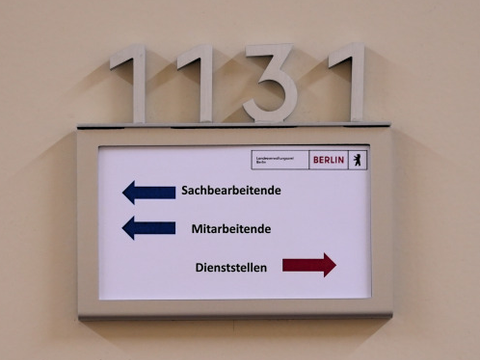 Ein Schild mit abgehenden Pfeilen von Sachbearbeitende, Mitarbeitende und Dienststellen an einer Tür