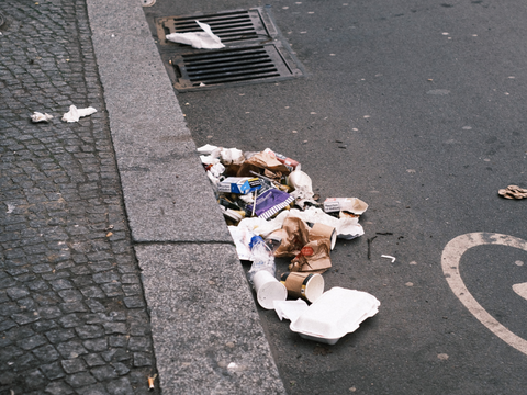 Am Straßenrand liegt achtlos weggeworfener Müll, eine Einwegverpackung und Servietten.