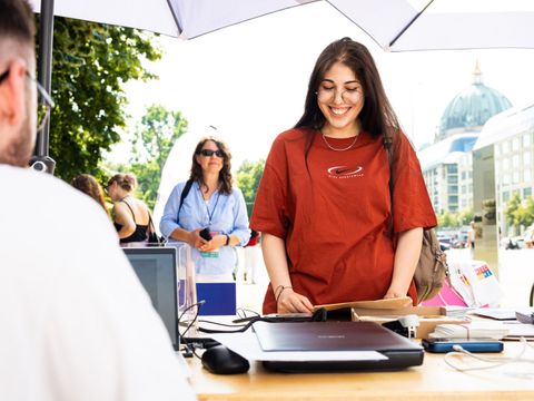 Lächelnde Frau steht vor Tisch mit Scanner, scheinbar bei einem Sommerfest