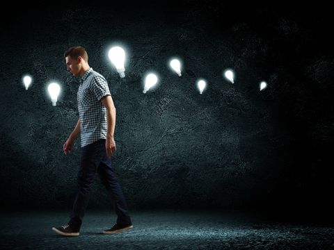 Laufender Mann vor dunklem Hintergrund mit mehreren Glühbirnen