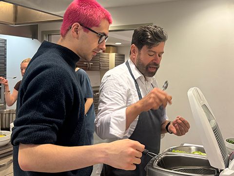 Kochkurs-Szene mit Jugendlichen und Kursleiter Michael Adrians: Erläuterung an der Friteuse