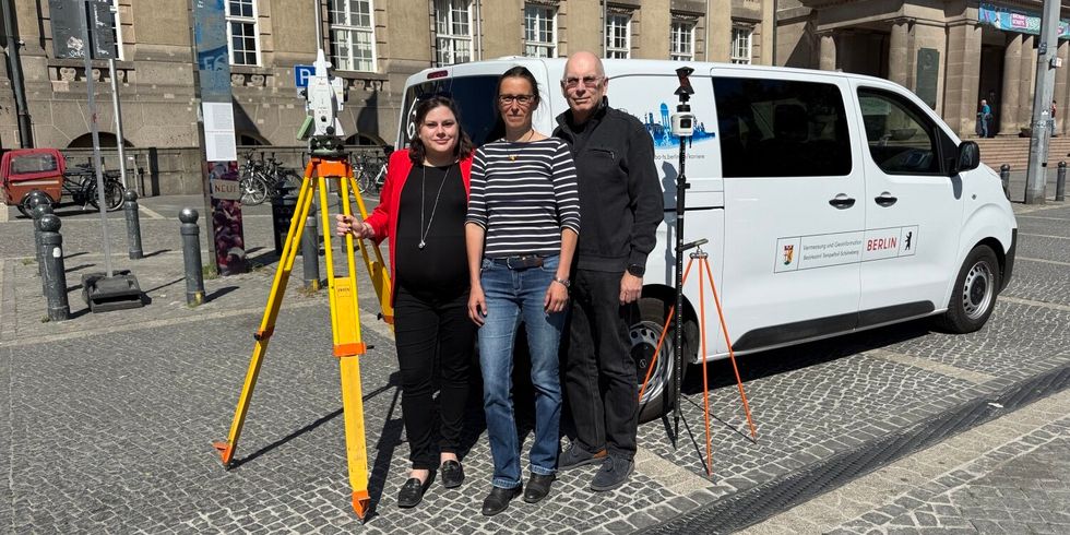 Drei Personen vor einem weißem Transporter mit Bezirksamtslogo und Vermessungsinstrumenten.