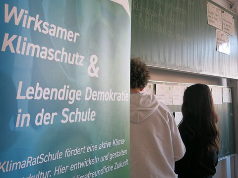 Plakat mit der Aufschrift wirksamer Klimaschutz zwei Personen stehen daneben