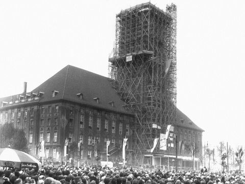 A large number of people are standing in a square in front of a large building.