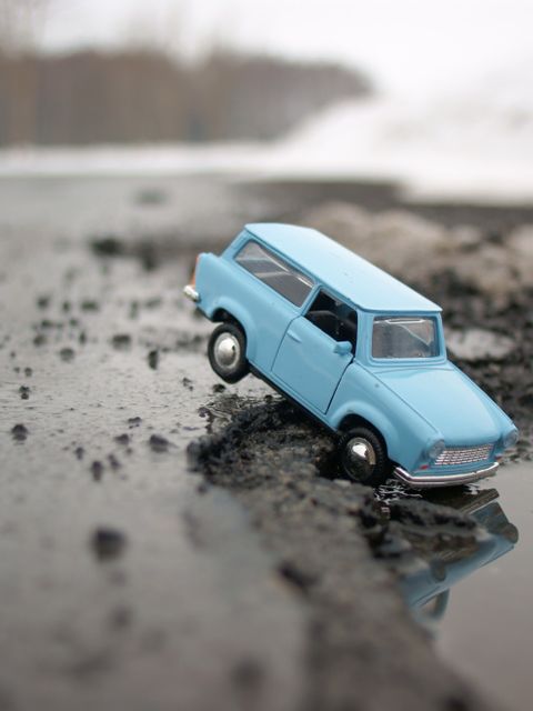 Ein Spielzeugtrabbi der in ein Schlagloch einer asphaltierten Straße hineinfällt