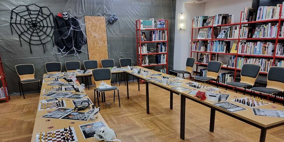 Das Foto zeigt mehrere Tische mit Schachbrettern darauf. Im Hintergrund sind Halloween-Schmuckelemente zu sehen.