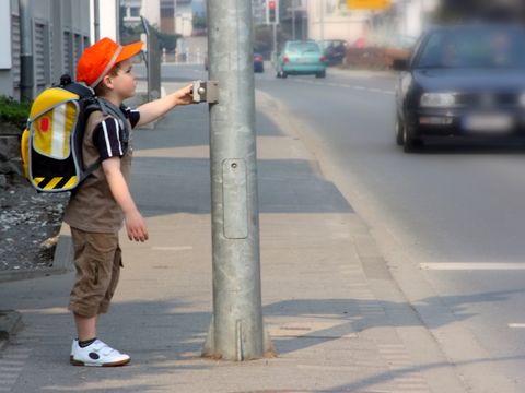 kleiner Schuljunge steht an einer Ampel um die Straße zu überqueren