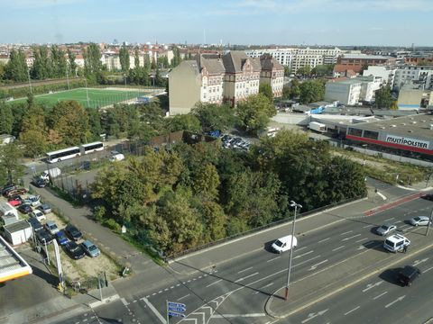 Vogelperspektive auf Grünfläche mit kleinem Bolzplatz sowie dreispurige Straße, Schulgebäude und Sportplatz im Hintergrund