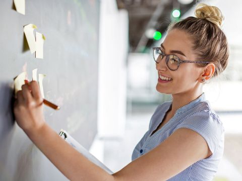 Vorbereitungsdienst - Junge Frau, die auf Post-Its an einer Tafel schreibt