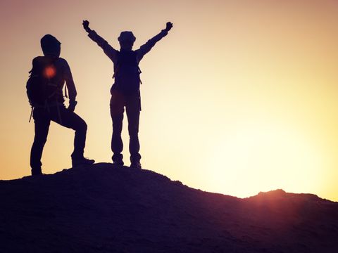 Zwei Personen stehen vor dem Sonnenaufgang auf einer Anhöhe und Freuen sich über einen Erfolg.