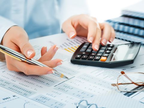 Hände mit Stift und Taschenrechner über Geschäftsunterlagen mit Tabellen