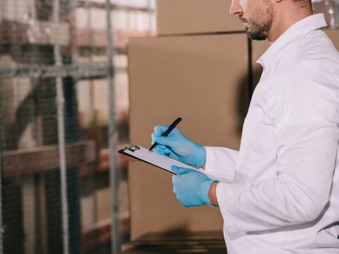 Ausgeschnittene Ansicht des Ladenbesitzers, der auf Klemmbrett in der Nähe von Kartons schreibt