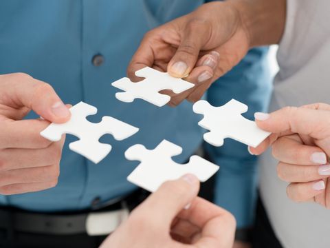 Vier Hände, die jeweils ein Puzzelteil halten