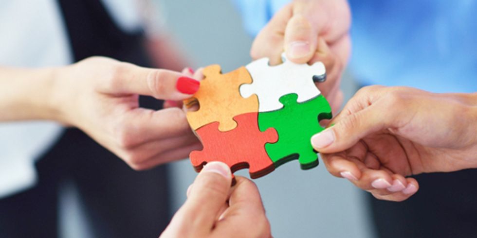 vier Hände stecken Puzzleteile zusammen