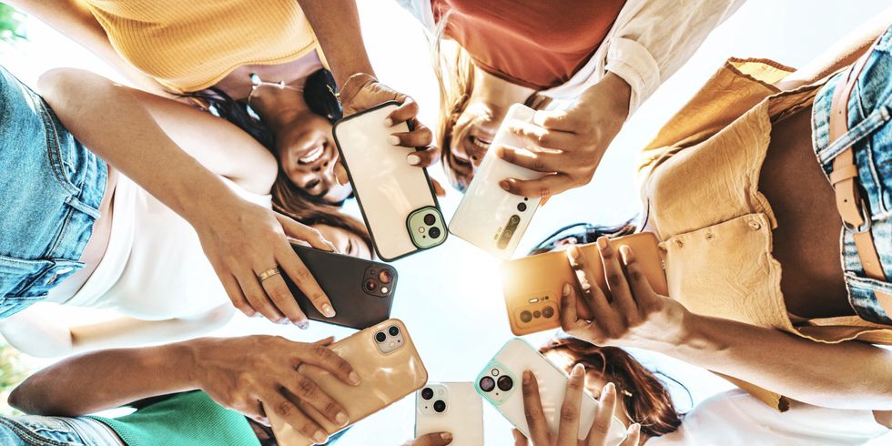 Gruppe junger Menschen, die draußen ein intelligentes Mobiltelefongerät benutzen, heller, farbenfroher Filter