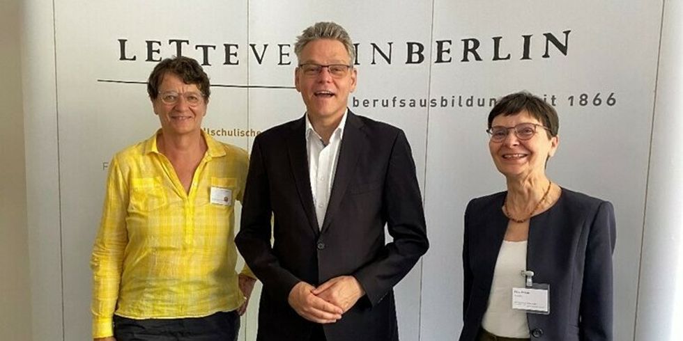 Zwei Frauen und ein Mann stehen vor einer Leinwand mit der Aufschrift Lette Verein Berlin