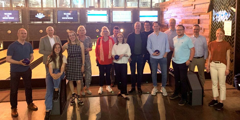 Eine Gruppe von Menschen steht vor einer Bowlingbahn. Manche halten Bowlingkugeln.