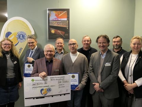 9 Menschen lächeln in die Kamera, einer hält einen großen Scheck für 5.000 €