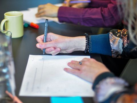 Eine Gruppe von Menschen die um einen Tisch sitzen und auf ein Blatt Papier schreiben