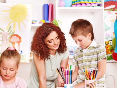 Das Bild zeigt eine Erzieherin und drei Kindern beim Basteln in einem Aufenthaltsraum