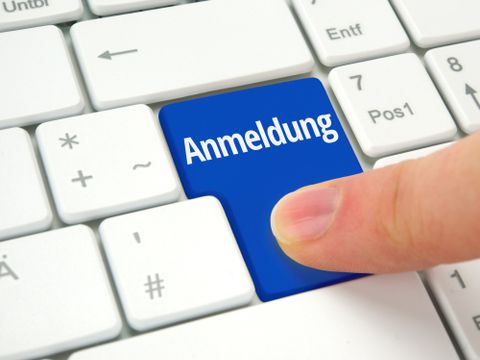 Zeigefinger wählt blaue Anmelde-Taste auf einer Tastatur aus