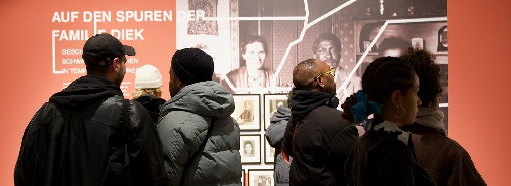 Menschen betrachten eine Wand mit Fotos und der Aufschrift „Auf den Spuren der Familie Diek"
