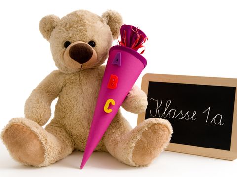 Teddybär mit einer Schultüte mit der Aufschrift "ABC" und einer Tafel auf der "Klasse 1a" steht