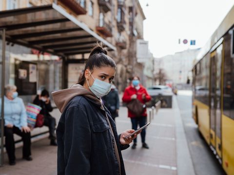 Junge Frau trägt Mundschutz an einer Bushaltestelle