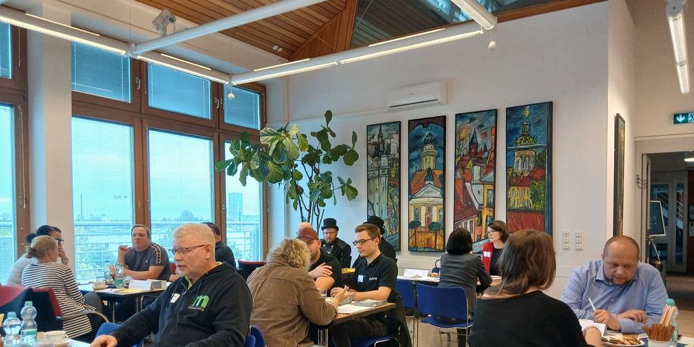 Teilnehmende im Gespräch an Tischen sitzend
