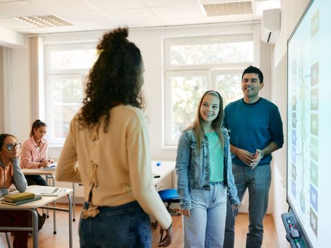 Schülerinnen und Lehrer stehen vor einem Smartboard