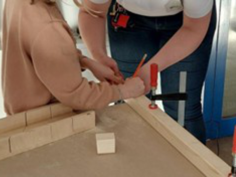 Eine größere und eine kleinere Person arbeiten zusammen an einer Holzwerkbank