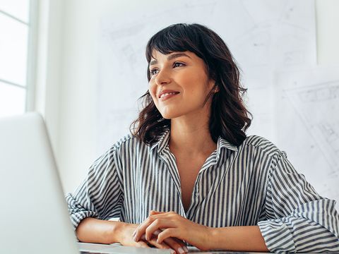 Frau mit Laptop vor ihr, im Hintergrund Architekturpläne