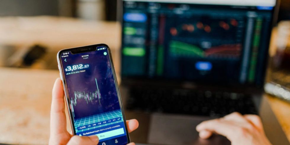 Hände halten ein Smartphone, auf dem Aktienkurse zu sehen sind