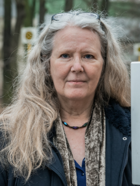 Eine Frau mit langen blonden Haaren schaut lächelnd in die Kamera.