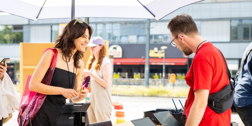 Lächelnde Frau interagiert mit männlichem Mitarbeiter, welcher vor Computern steht