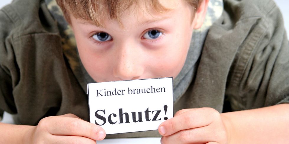 Junge hält Zettel mit Aufschrift: Kinder brauchen Schutz