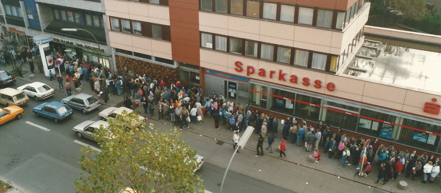 Viele Menschen stehen wartend auf einem Bürgersteig